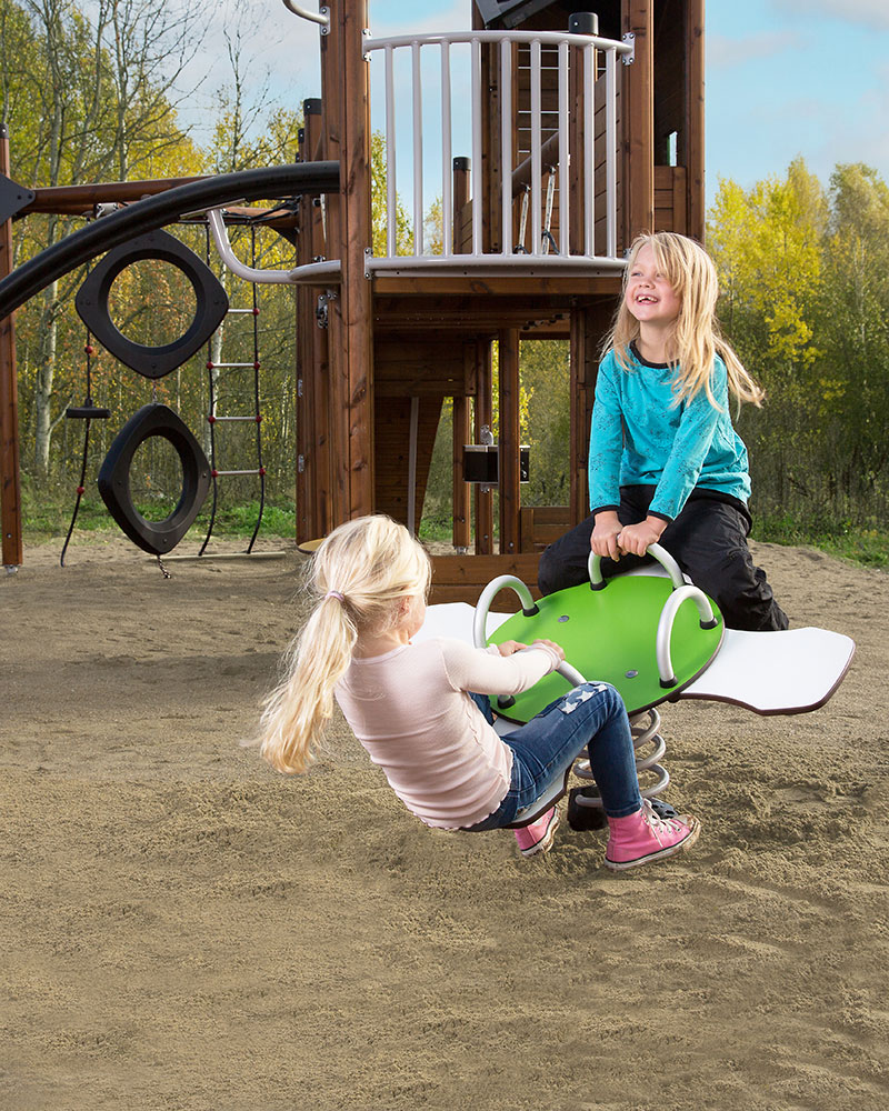 2 young children are playing on a seesaw which is shaped like a cross with 4 seats. They are laughing and in motion.